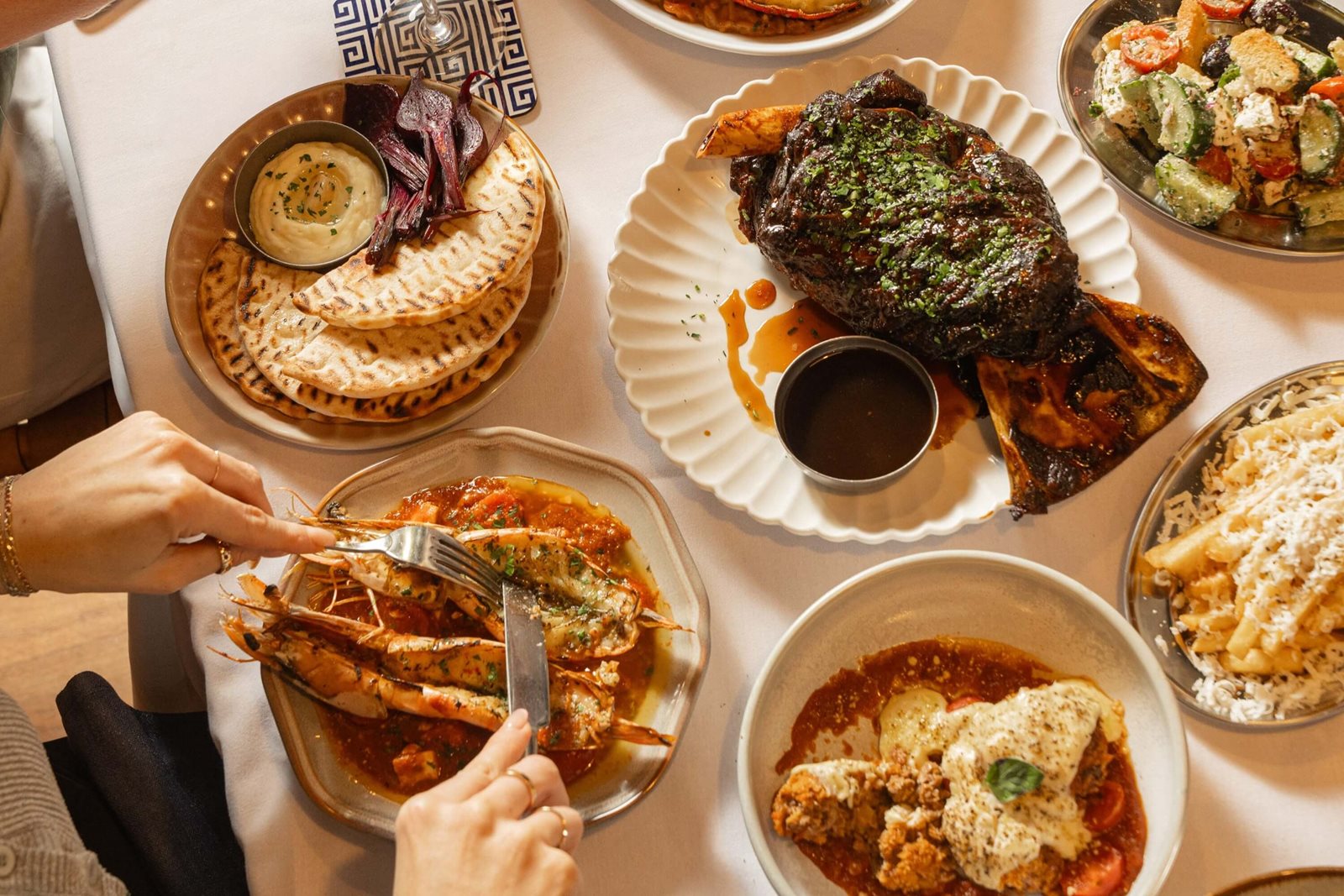 A shared Greek table with pita, prawns, lamb, salad, and fries at Jimmy's Kitchen Bay Nine