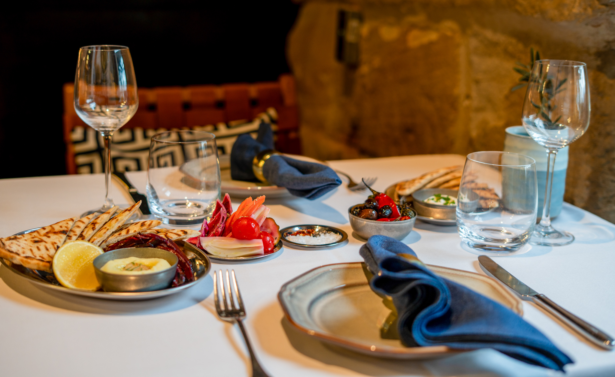 A table set with pita, dips, wine glasses, and warm sandstone at Jimmy's Kitchen Bay Nine